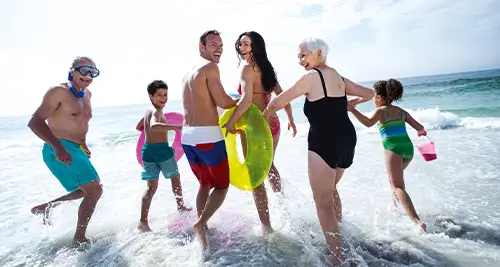 Famille intergénérationnelle courant vers la mer sur une plage, idéale pour un séjour dans un village vacances VTF en France