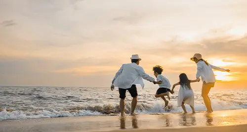 Famille avec deux enfants courant vers la mer au coucher du soleil, moment complice des villages vacances France en bord de plage