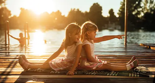 Deux jeunes filles assises sur un ponton au bord d’un lac, pendant des vacances en village VTF en pleine nature