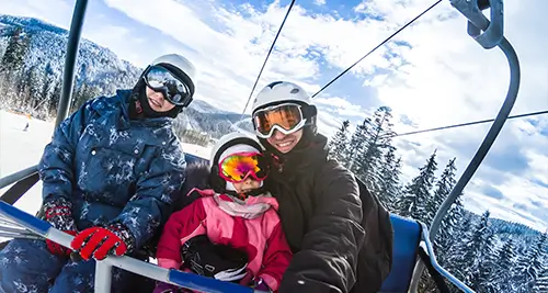 Maman prenant un selfie avec ses enfants sur un télésiège, ambiance de village de vacances ski à la montagne
