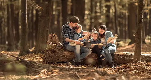 Famille avec deux enfants lisant des livres dans une forêt calme proche d'un village vacances France VTF